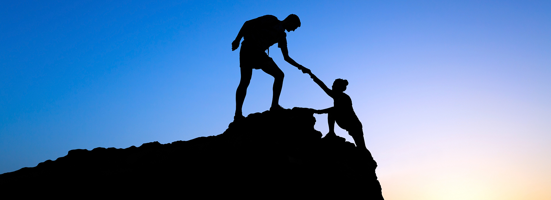 Image of a person on a mountain pulling up another person up 